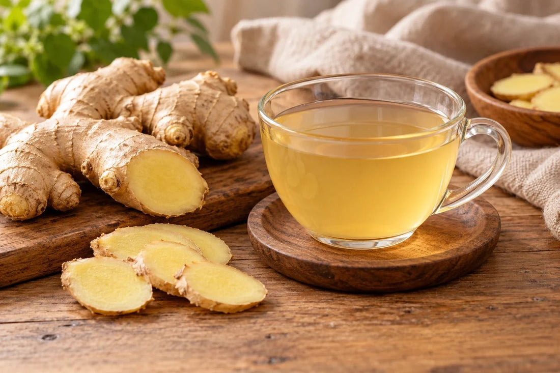 Fresh ginger roots and slices beside a clear cup of ginger infusion